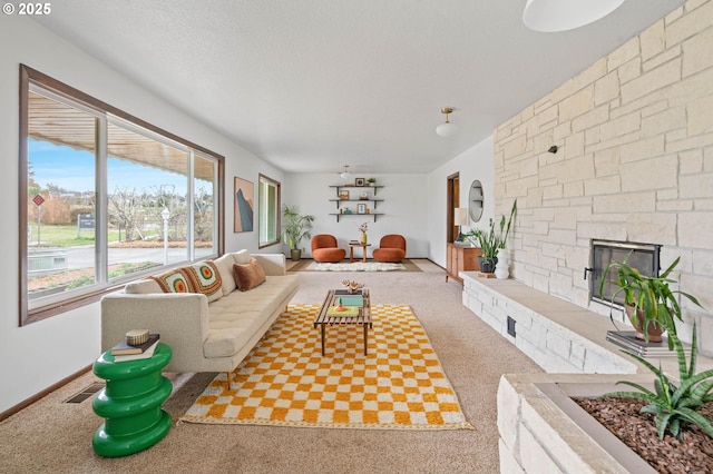 carpeted living area with visible vents, baseboards, a textured ceiling, and a stone fireplace