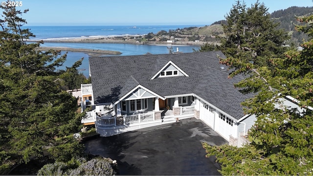 view of front facade with aphalt driveway, roof with shingles, a garage, and a water view