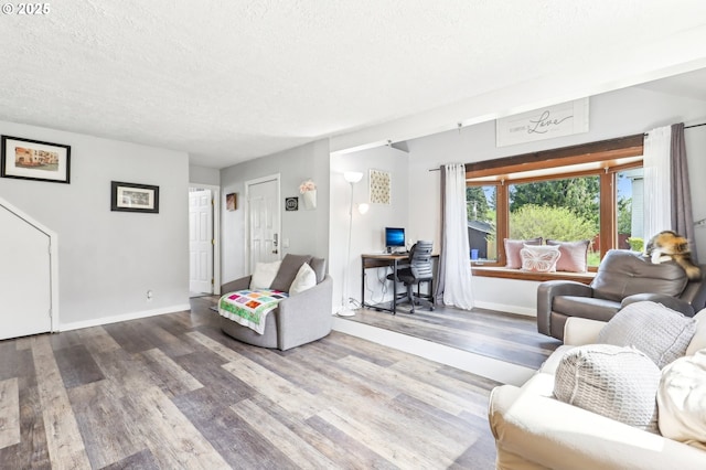 living area with baseboards, a textured ceiling, and wood finished floors
