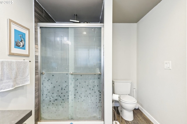 bathroom with toilet, baseboards, wood finished floors, and a stall shower