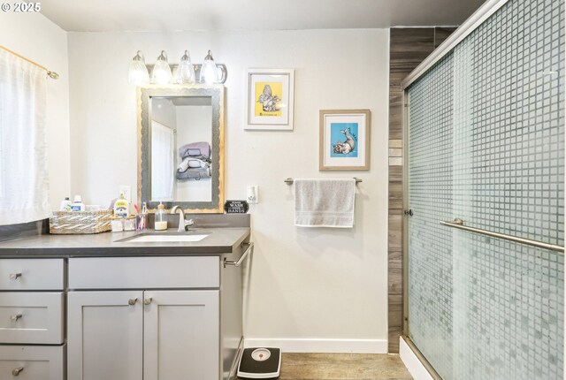 bathroom featuring vanity, baseboards, wood finished floors, and a stall shower