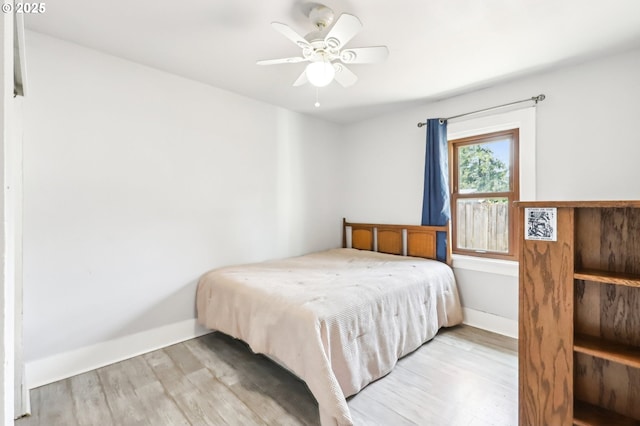 bedroom with light wood-type flooring, a ceiling fan, and baseboards