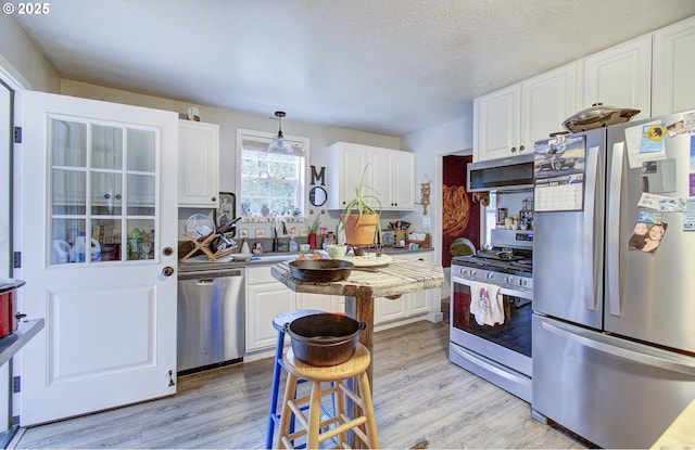 116 SE Williams Rd, Gresham, OR 97080 - kitchen with appliances with stainless steel finishes, white cabinetry, light wood-type flooring, decorative light fixtures, and light countertops
