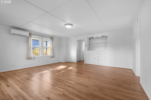 empty room featuring built in shelves, light hardwood / wood-style flooring, and an AC wall unit