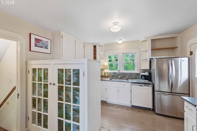 kitchen featuring freestanding refrigerator, dishwashing machine, open shelves, a sink, and light wood-type flooring