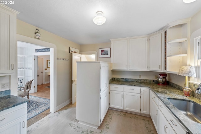 kitchen with a sink, open shelves, light wood-style floors, dark stone countertops, and white cabinets