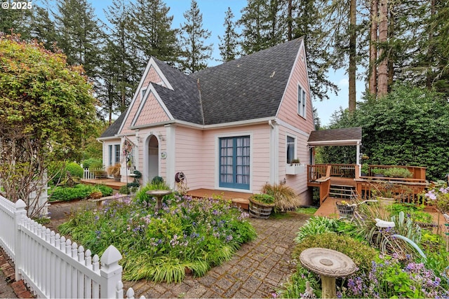 view of front facade with a wooden deck, a shingled roof, fence, and a patio area