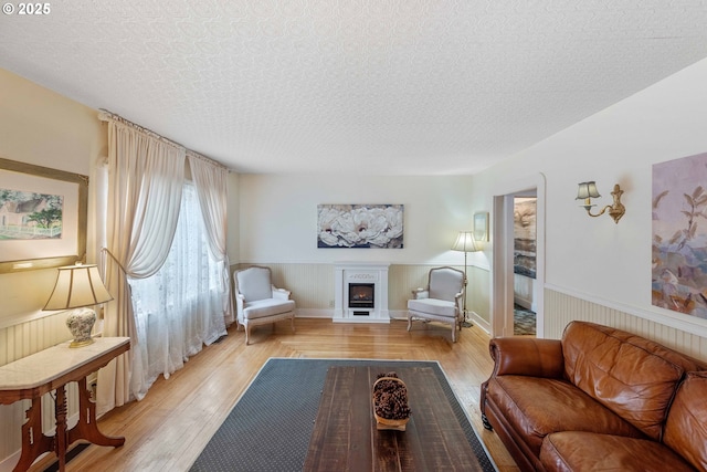 living area featuring a wainscoted wall, a warm lit fireplace, light wood-style floors, and a textured ceiling