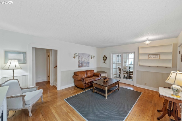 living area with a wainscoted wall, light wood finished floors, and stairway