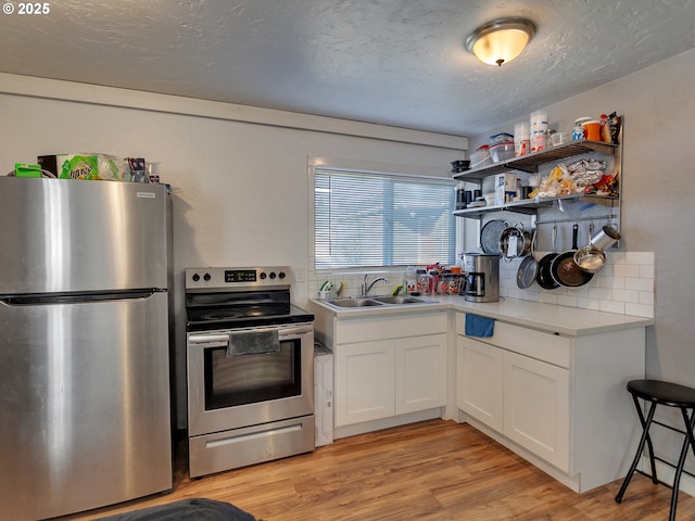 kitchen with appliances with stainless steel finishes, sink, white cabinetry, and light wood-type flooring