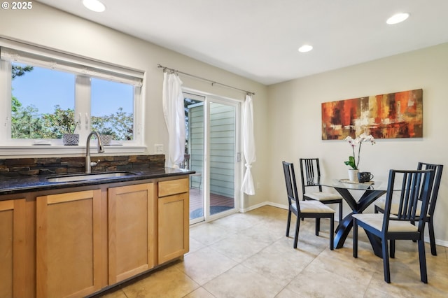 kitchen featuring a sink, light tile patterned flooring, recessed lighting, dark stone counters, and baseboards