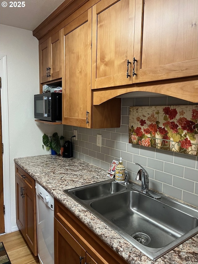 kitchen featuring a sink, backsplash, black microwave, light wood finished floors, and dishwasher