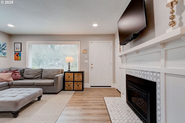 living room featuring a tile fireplace, a textured ceiling, and light wood-type flooring