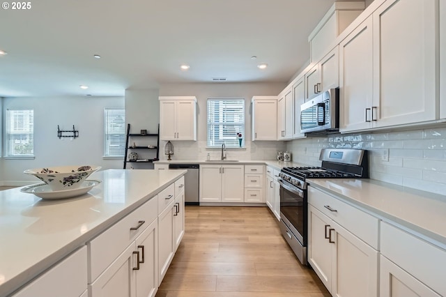 12935 SW Tabor Ter, Beaverton, OR 97007 - kitchen with appliances with stainless steel finishes, white cabinets, decorative backsplash, light wood finished floors, and light countertops