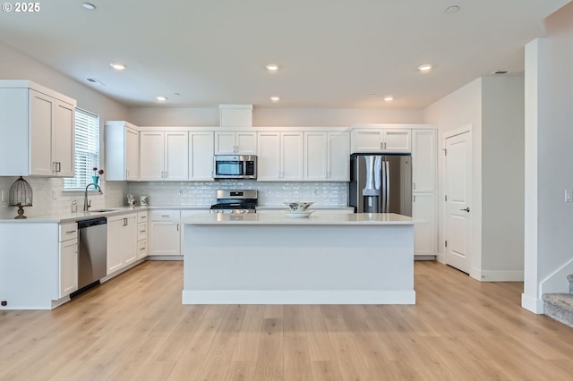 12935 SW Tabor Ter, Beaverton, OR 97007 - kitchen with appliances with stainless steel finishes, a center island, light countertops, white cabinets, and light wood finished floors