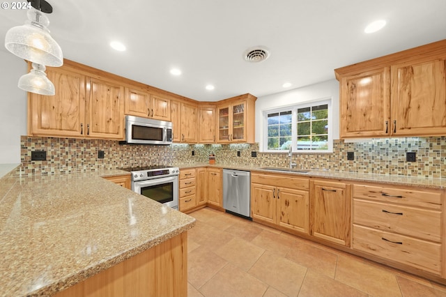 kitchen featuring appliances with stainless steel finishes, a sink, backsplash, and light stone countertops