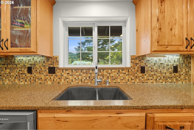 kitchen with a sink, backsplash, stainless steel dishwasher, and light stone countertops