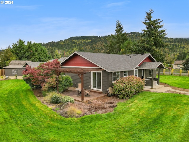 view of front of home with a pergola, roof with shingles, a patio area, a wooded view, and a front yard