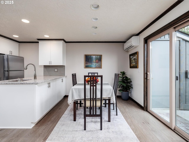 dining room with a wall mounted air conditioner, a textured ceiling, ornamental molding, and light wood finished floors