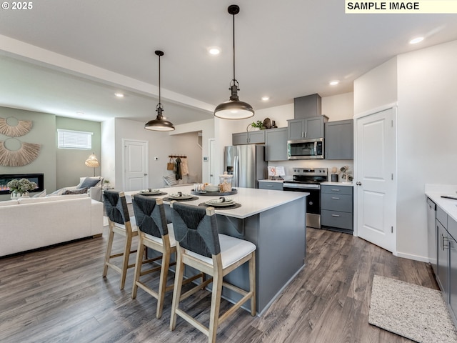 kitchen featuring gray cabinetry, light countertops, stainless steel appliances, open floor plan, and a breakfast bar area