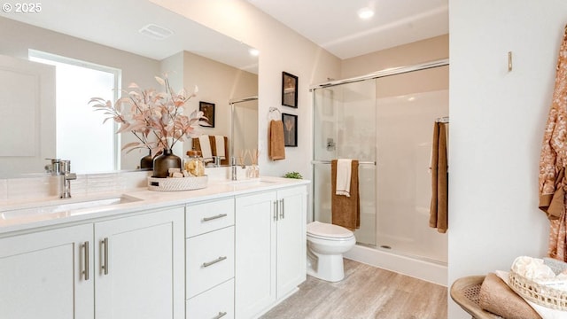 bathroom featuring a stall shower, double vanity, a sink, and wood finished floors