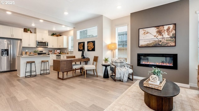 interior space with a center island, appliances with stainless steel finishes, a glass covered fireplace, light wood-style floors, and white cabinetry