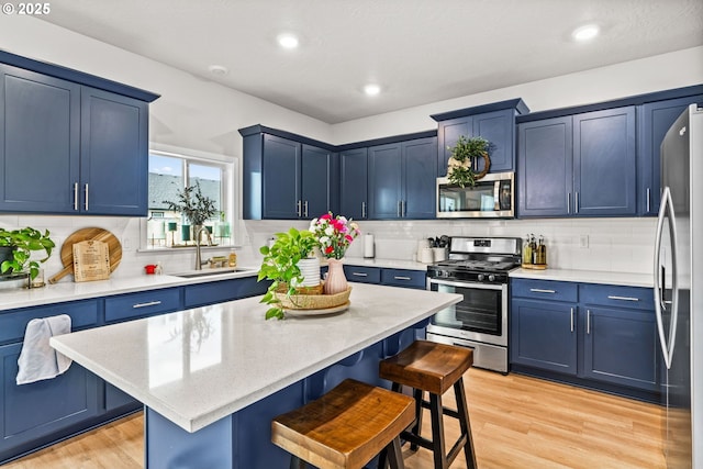 kitchen featuring stainless steel appliances, a sink, a breakfast bar, blue cabinetry, and light wood finished floors