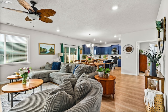 living area with light wood-type flooring, ceiling fan, baseboards, a chandelier, and a textured ceiling
