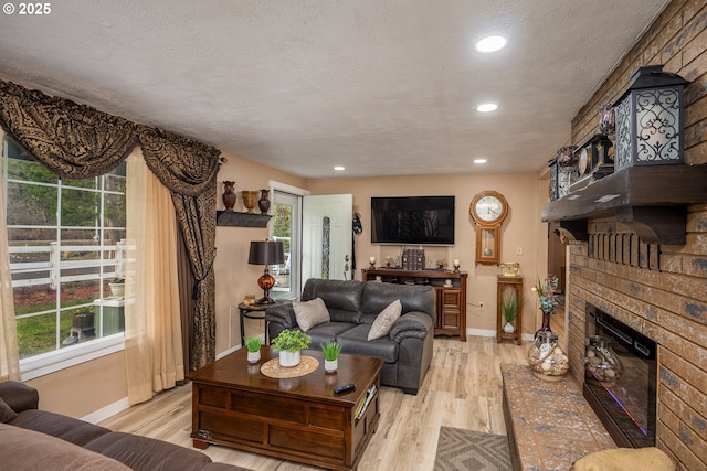 living room featuring light wood-style floors, a fireplace, a textured ceiling, and baseboards