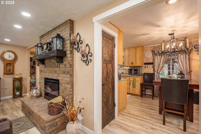 living area featuring a textured ceiling, a chandelier, light wood-style flooring, baseboards, and a brick fireplace