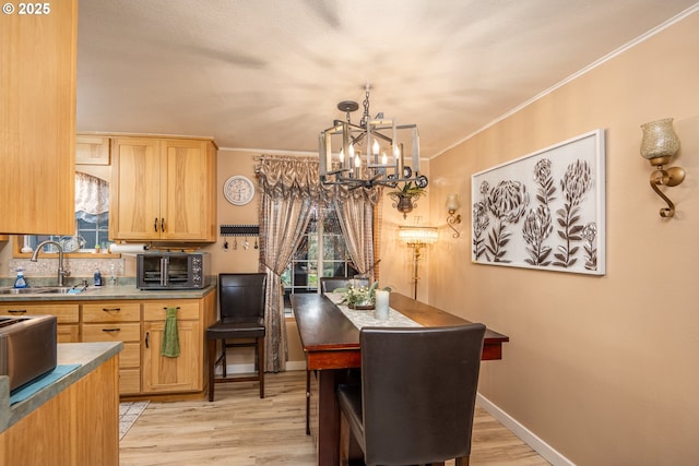 kitchen with light wood finished floors, crown molding, baseboards, and a sink