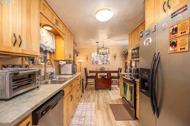 kitchen featuring a toaster, stainless steel appliances, a sink, hanging light fixtures, and light wood-type flooring