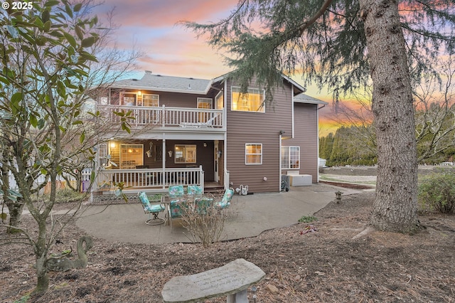 back house at dusk featuring a patio area and a balcony