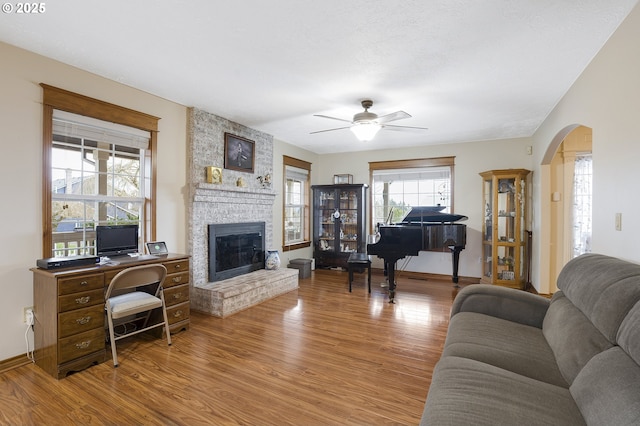 living room featuring ceiling fan, wood-type flooring, and a brick fireplace