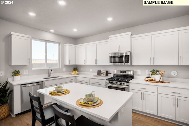4321 Dogwood Ave, Albany, OR 97322 - kitchen with stainless steel appliances, a sink, wood finished floors, a kitchen bar, and white cabinets