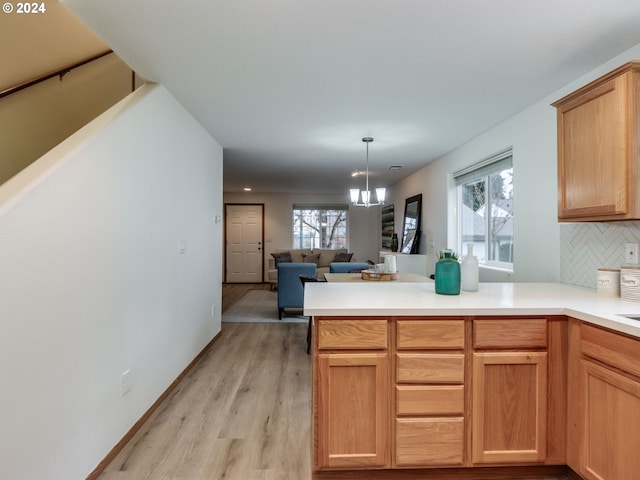 kitchen with backsplash, plenty of natural light, kitchen peninsula, a chandelier, and light wood-type flooring