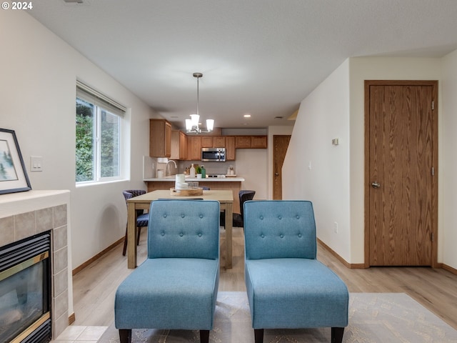 dining room featuring sink, light hardwood / wood-style floors, a tile fireplace, and a notable chandelier