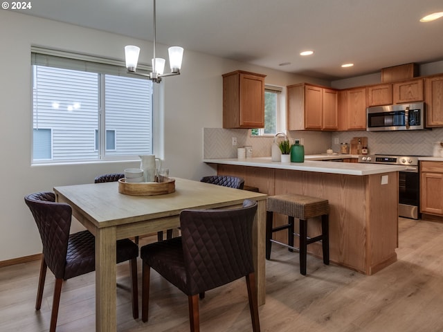 kitchen featuring appliances with stainless steel finishes, decorative light fixtures, tasteful backsplash, a kitchen bar, and light wood-type flooring