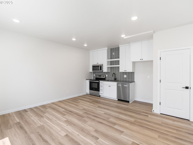 kitchen with backsplash, sink, light hardwood / wood-style flooring, white cabinetry, and stainless steel appliances