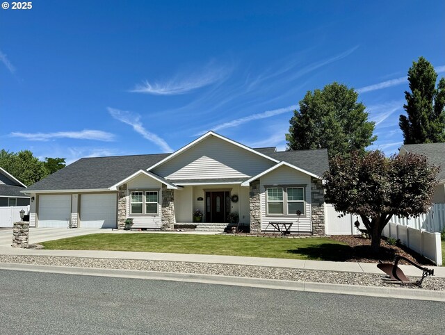 view of front of property featuring a front lawn, fence, a garage, stone siding, and driveway