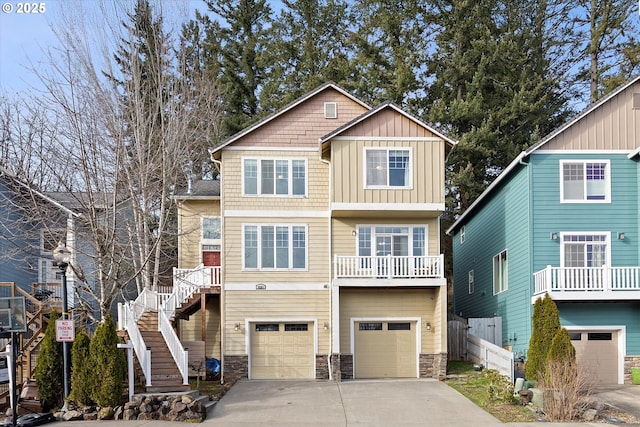 view of front of home with an attached garage, driveway, stone siding, stairway, and board and batten siding