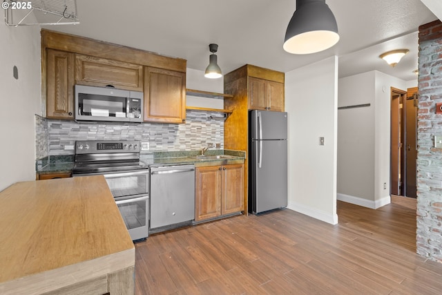 kitchen featuring appliances with stainless steel finishes, pendant lighting, tasteful backsplash, wood-type flooring, and sink