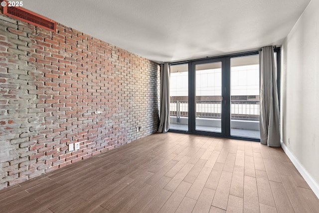 unfurnished room with hardwood / wood-style floors, a wall of windows, and brick wall