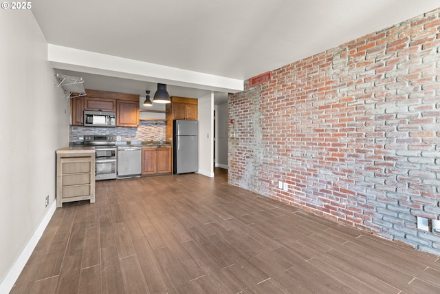 kitchen with brick wall, appliances with stainless steel finishes, sink, decorative backsplash, and hardwood / wood-style flooring