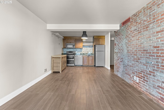 kitchen featuring hardwood / wood-style flooring, brick wall, appliances with stainless steel finishes, and tasteful backsplash