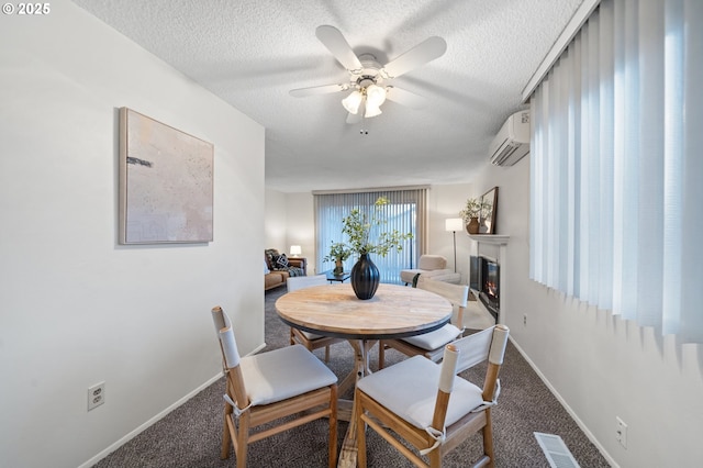 carpeted dining room with a textured ceiling, a wall unit AC, a ceiling fan, baseboards, and a glass covered fireplace