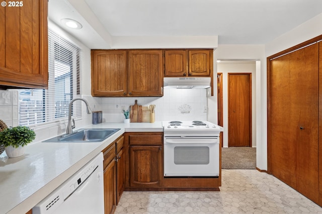 kitchen with under cabinet range hood, white appliances, a sink, light countertops, and brown cabinets