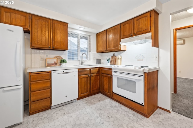 kitchen with white appliances, brown cabinetry, light countertops, under cabinet range hood, and a sink