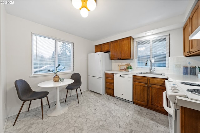 kitchen featuring white appliances, brown cabinets, a sink, light countertops, and backsplash