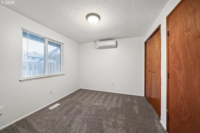 unfurnished bedroom with dark colored carpet, visible vents, a wall mounted AC, a textured ceiling, and baseboards